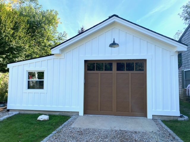 White-sided garage with brown garage door, gravel path, and small window.
