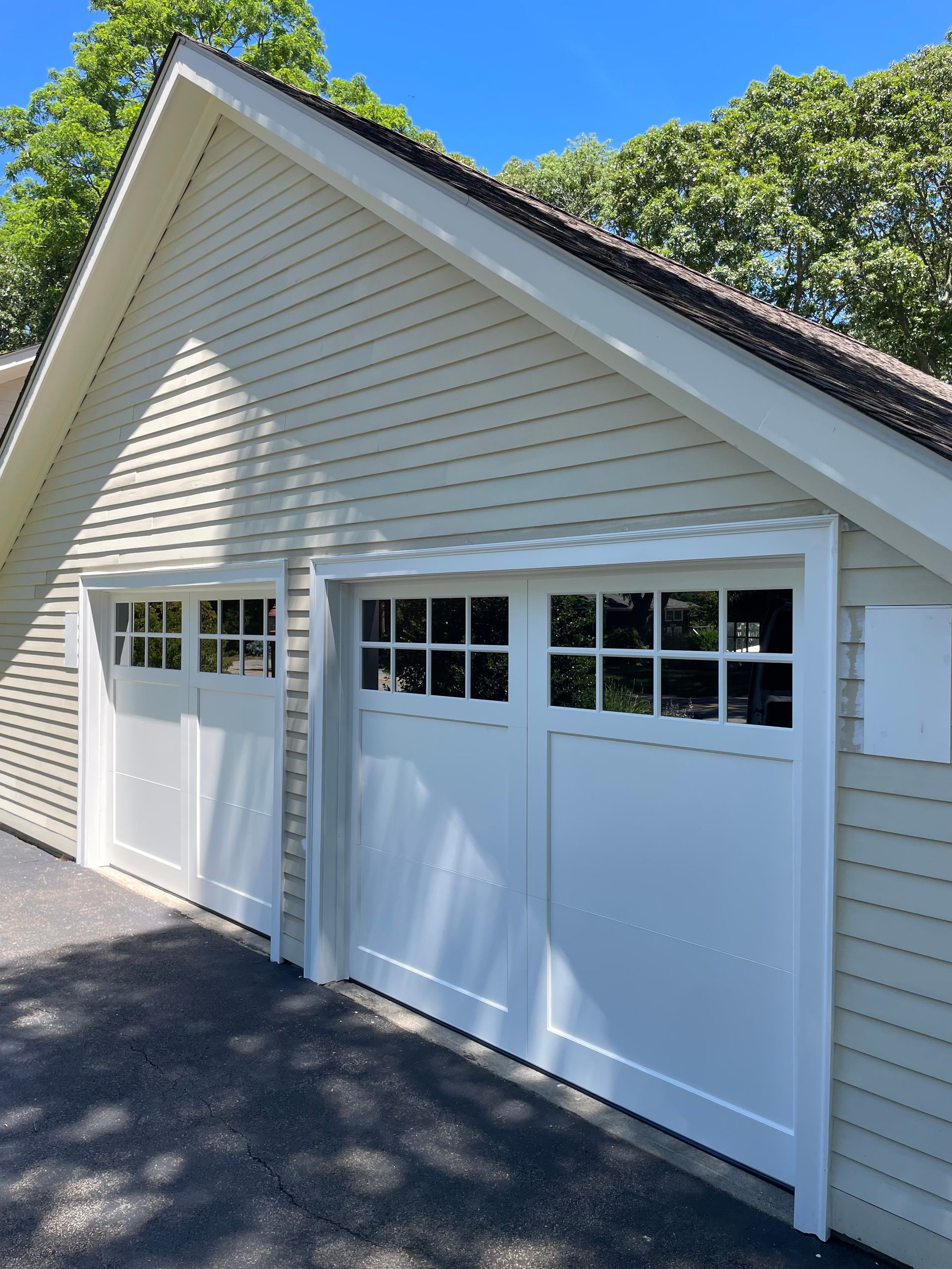 White garage doors with windows on a light green clapboard house under a blue sky.