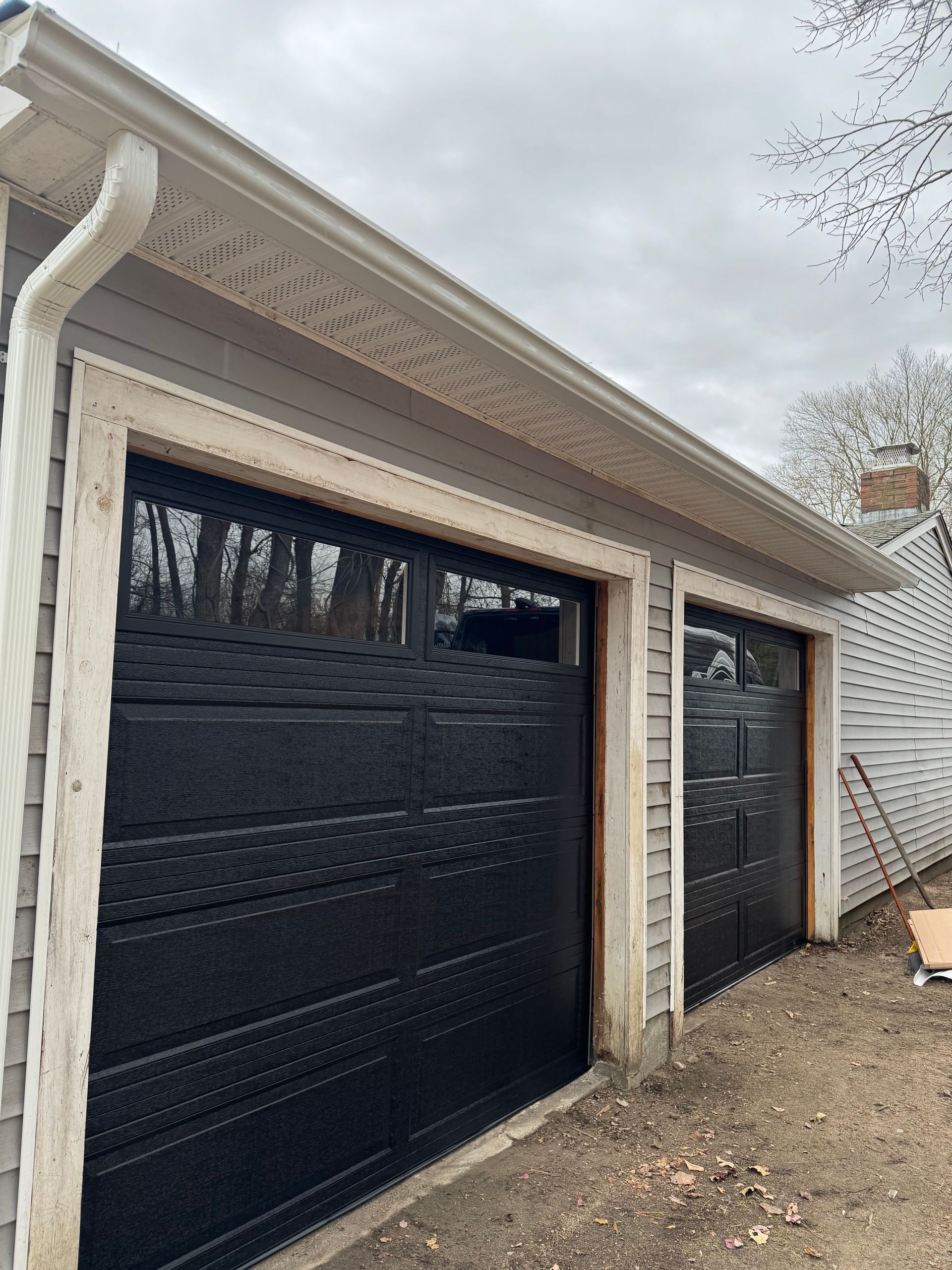 Two black garage doors with light trim and gray siding under a cloudy sky.