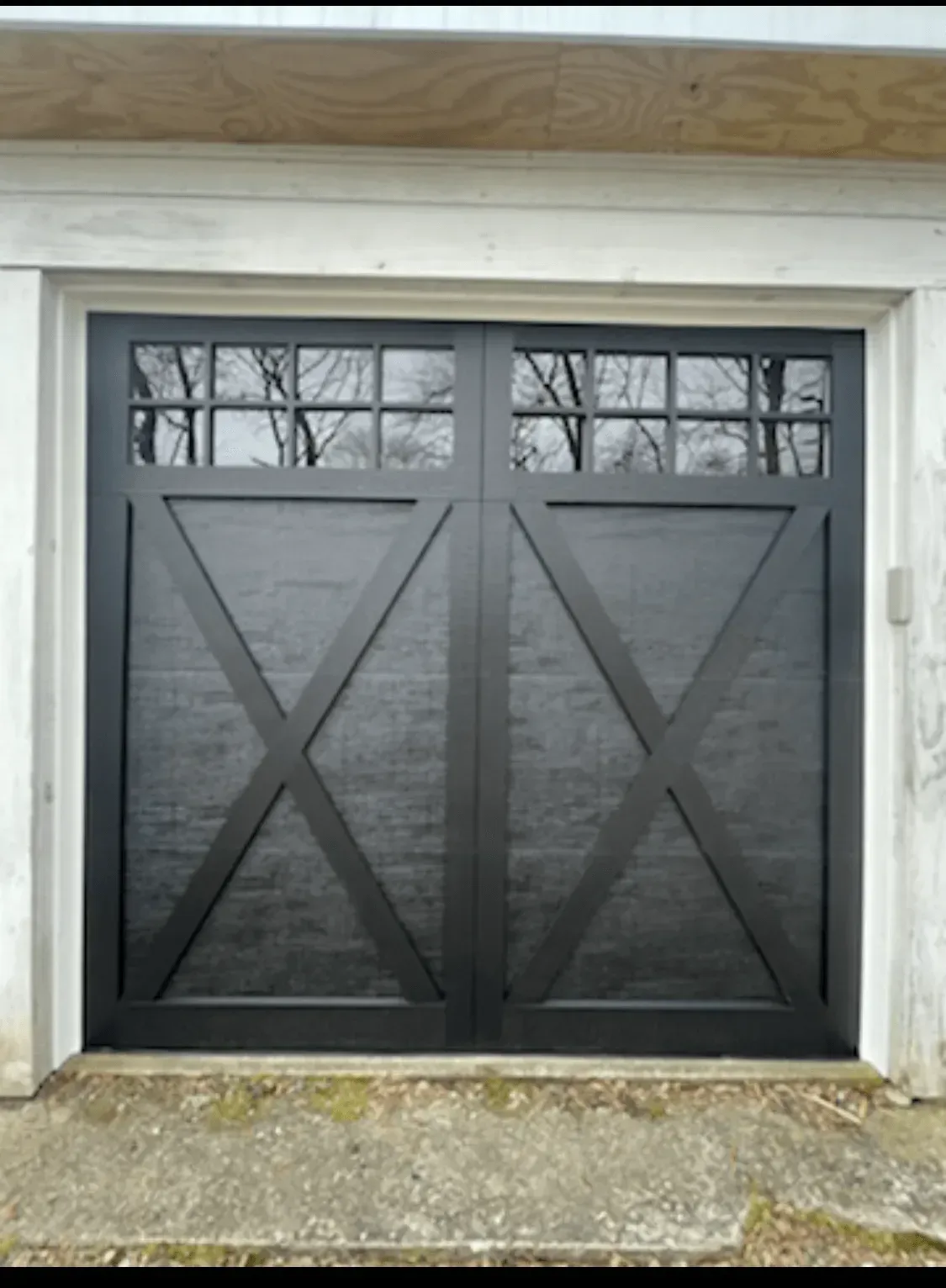 Black garage door with windowed top and crisscross design.