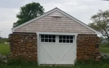 Garage with stone foundation and white door, under a cedar-shingled gable roof.