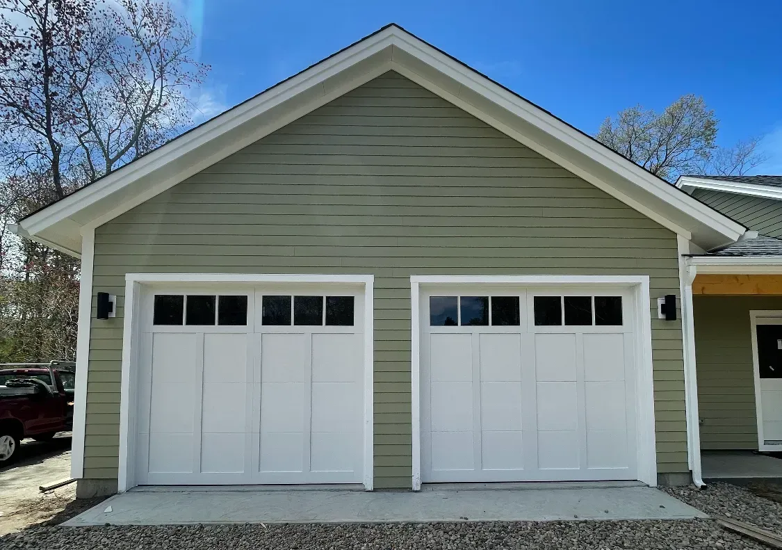 Two-car garage with white doors, green siding, and white trim against a blue sky.