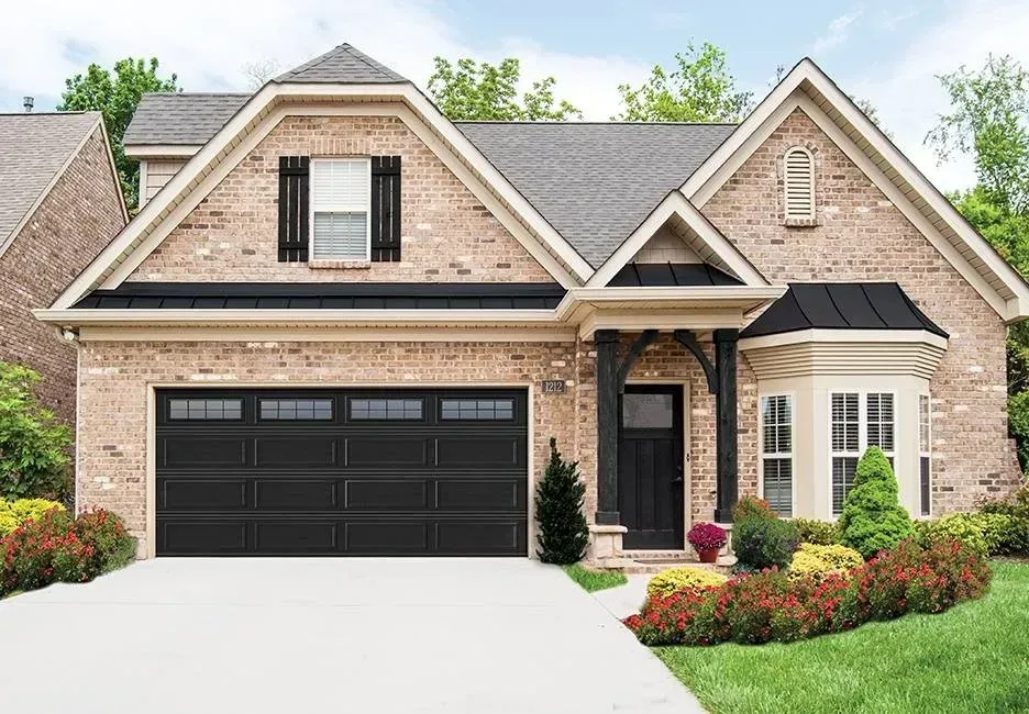 Black garage door on a brick house with a front porch, and landscaped yard.