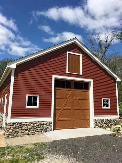 Red barn with brown garage door, white trim, stone foundation, and a blue sky.