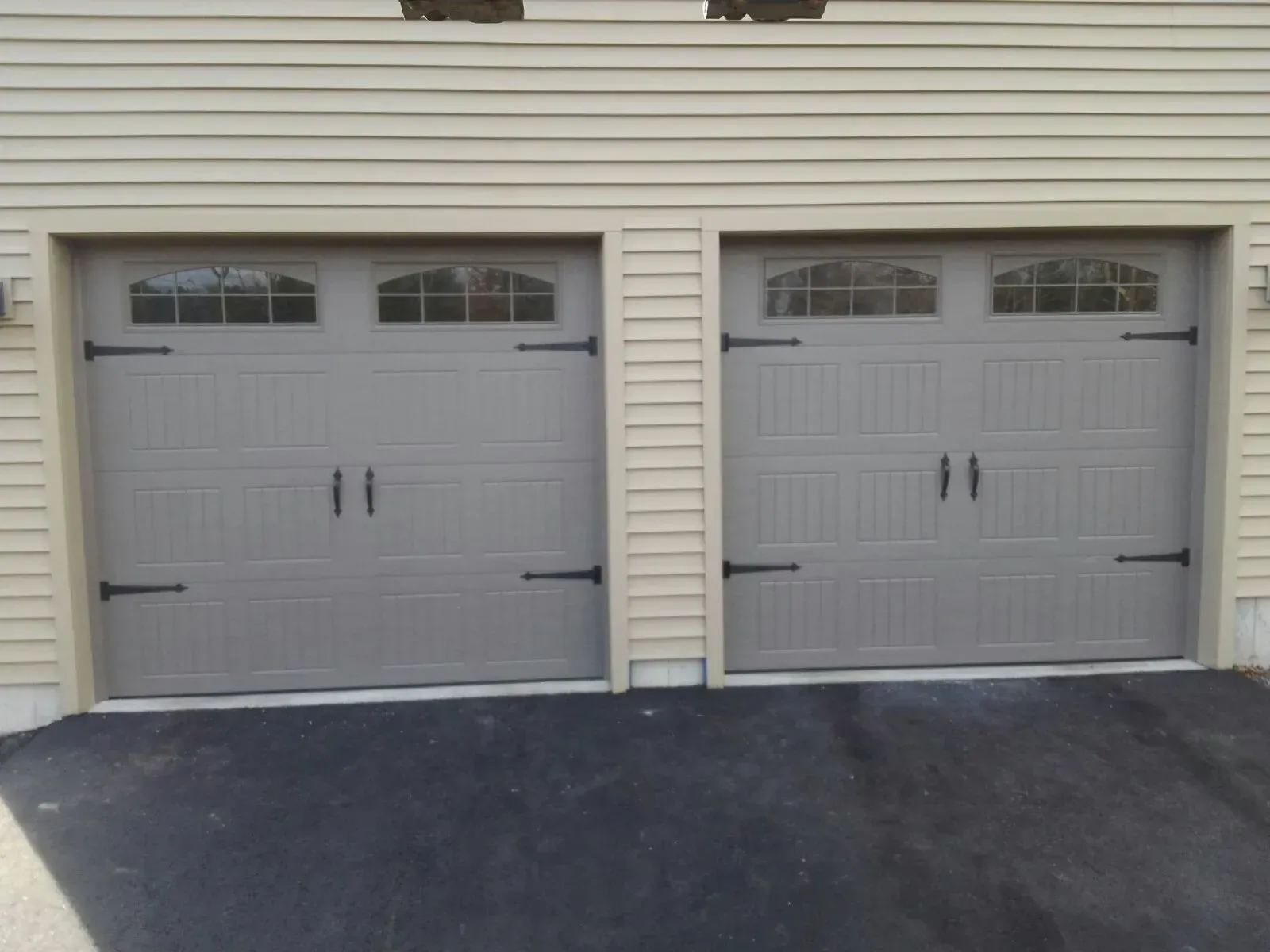 Two gray garage doors with decorative black hardware, set in a light beige building.