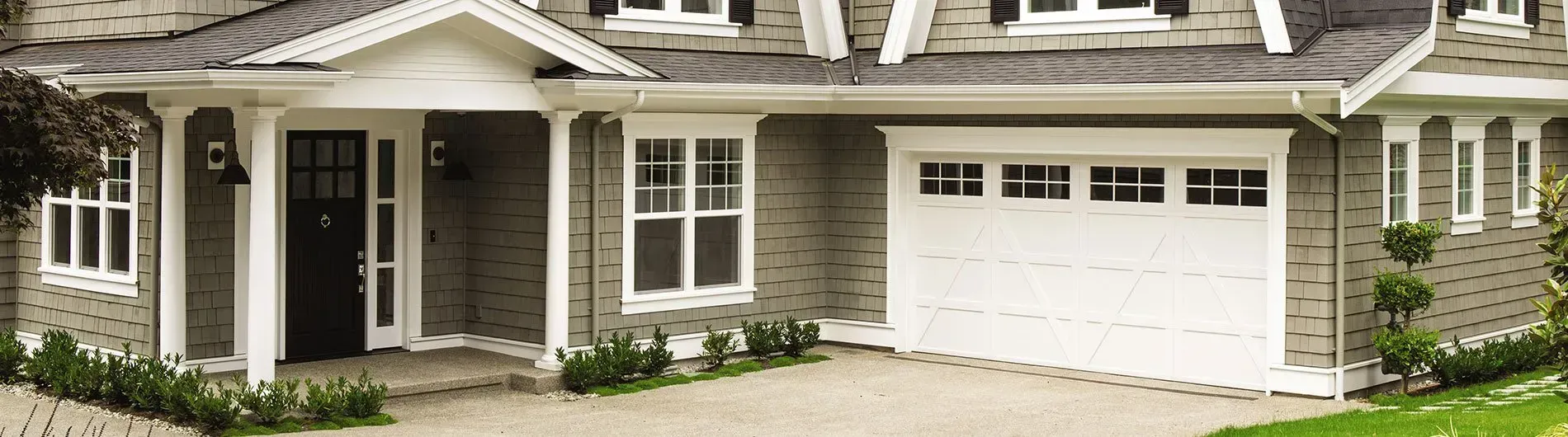 Exterior view of a house with a white garage door, black front door, and a gravel driveway.