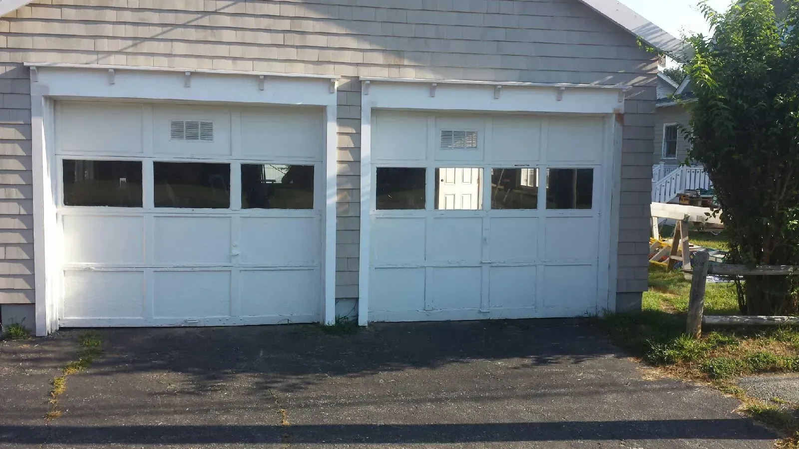 White double garage doors with small rectangular windows, in front of a gray building, with asphalt driveway.