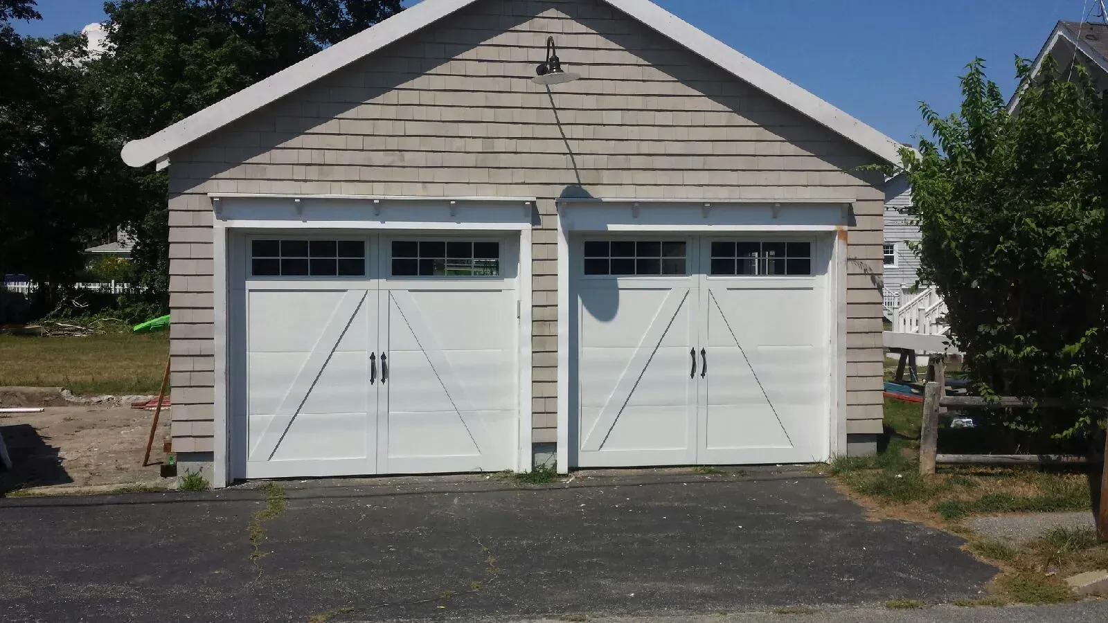 Two white garage doors on a light gray shingled building with a dark driveway.
