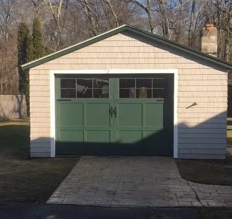 Green garage door with windows, on a shingled building, green trim.
