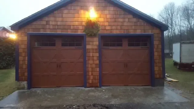 Brown double garage with wood shingle siding and dark blue trim. Wet concrete driveway.
