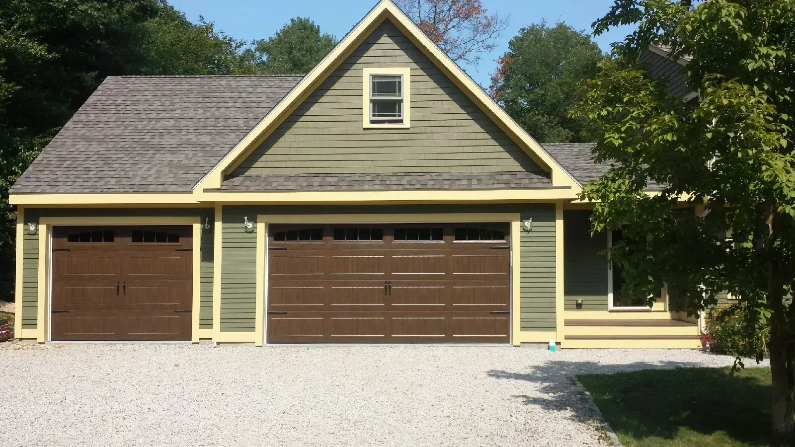 Two-car garage with brown doors, light green siding, and a gabled roof. Beige trim surrounds the building.