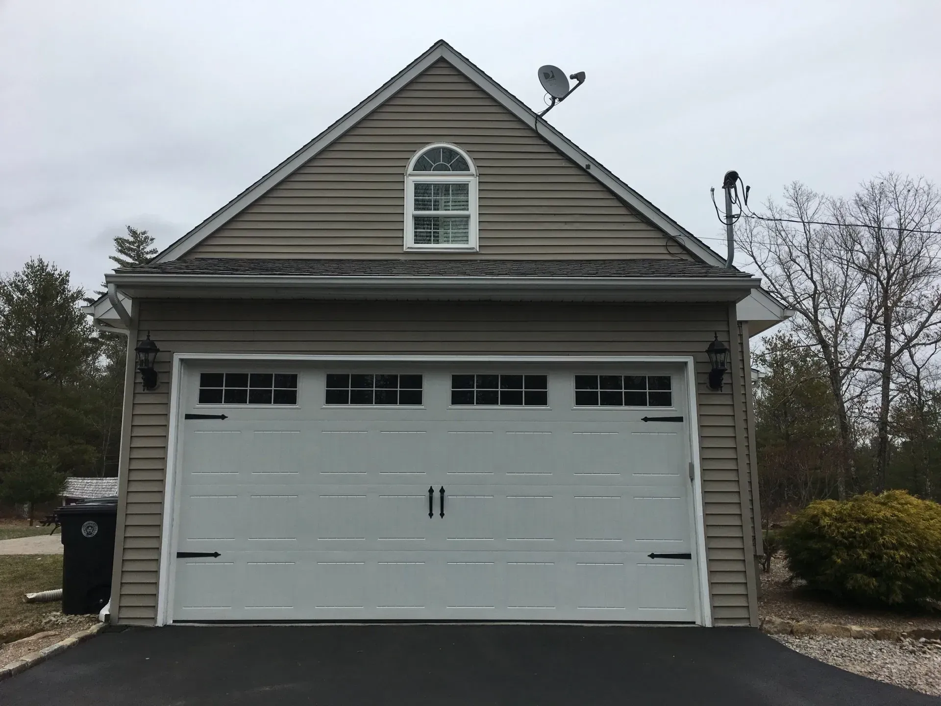 White garage door on a beige two-story building with a small arched window. Satellite dish on the roof.