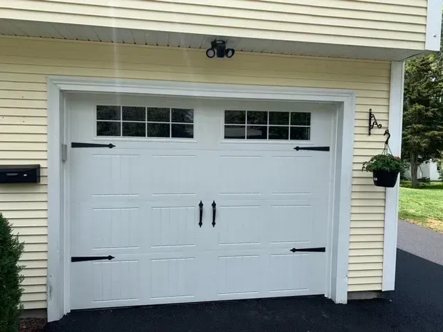 White garage door with windows, decorative black hardware, and yellow siding.