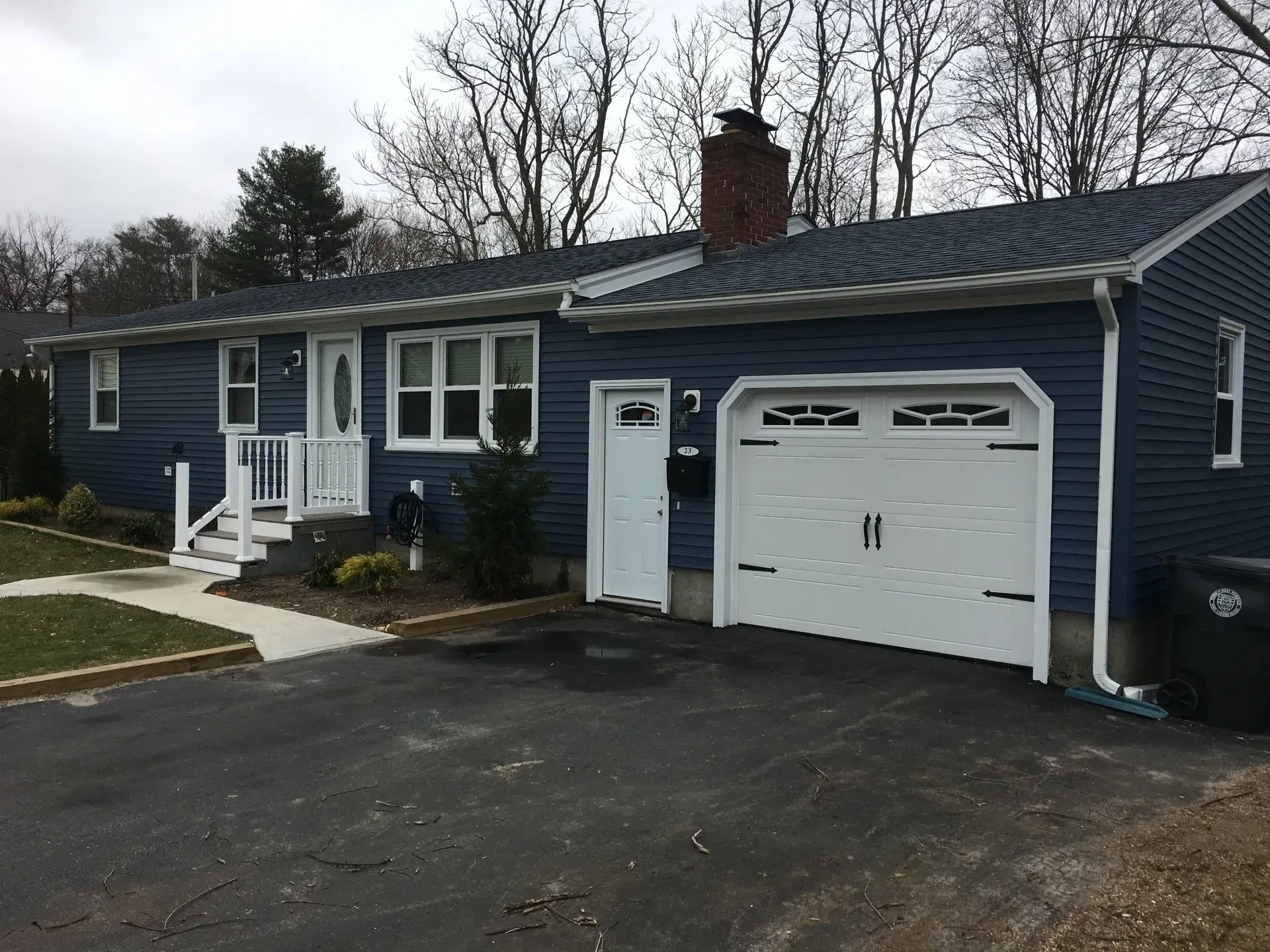 Blue-sided, one-story house with white trim, a garage, and a driveway on a cloudy day.