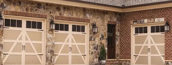 Three tan garage doors with white accents and a stone and brick exterior.