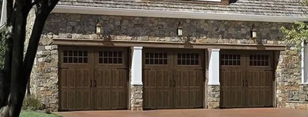 Three wooden garage doors with stone facade and decorative lighting.