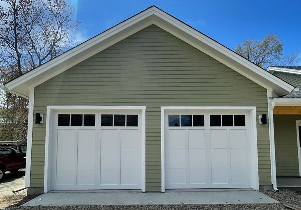 Two white garage doors on a green house with white trim and black lights.