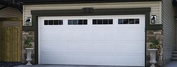 White garage door with windows, flanked by stone columns, lights, and planters.