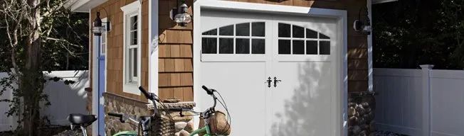 White garage door with arched window. Brown siding and stone pillars. Two bicycles in front.
