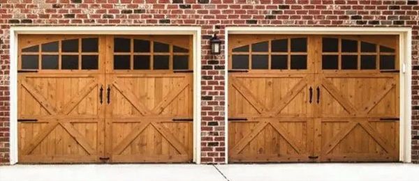 Two wooden garage doors with arched top windows, on a brick building.