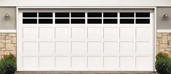 White garage door with windows, stone accent walls, and bushes.