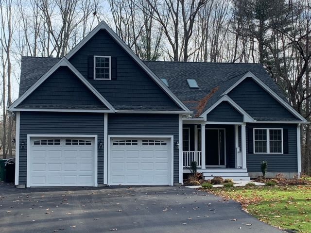 Blue-sided house with white garage doors and a front porch, set in front of bare trees and a driveway.