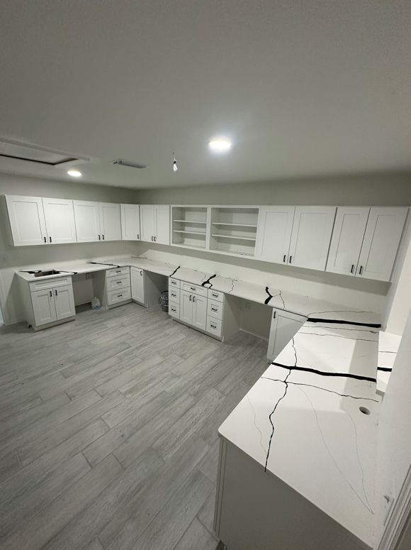 A kitchen with white cabinets and marble counter tops.