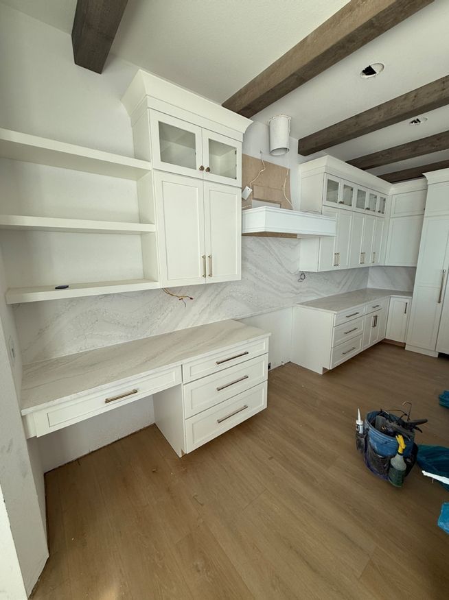 A kitchen with white cabinets and wooden floors and a desk.