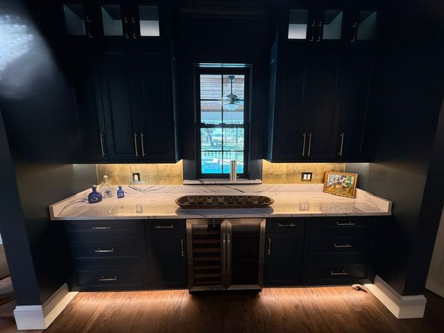 A kitchen with black cabinets , a sink , a refrigerator and a window.