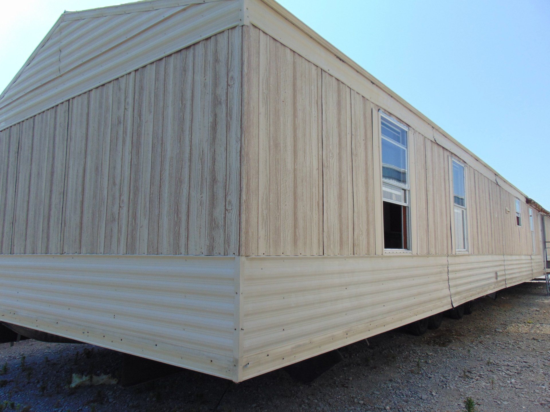 A mobile home is sitting in a gravel lot with a blue sky in the background