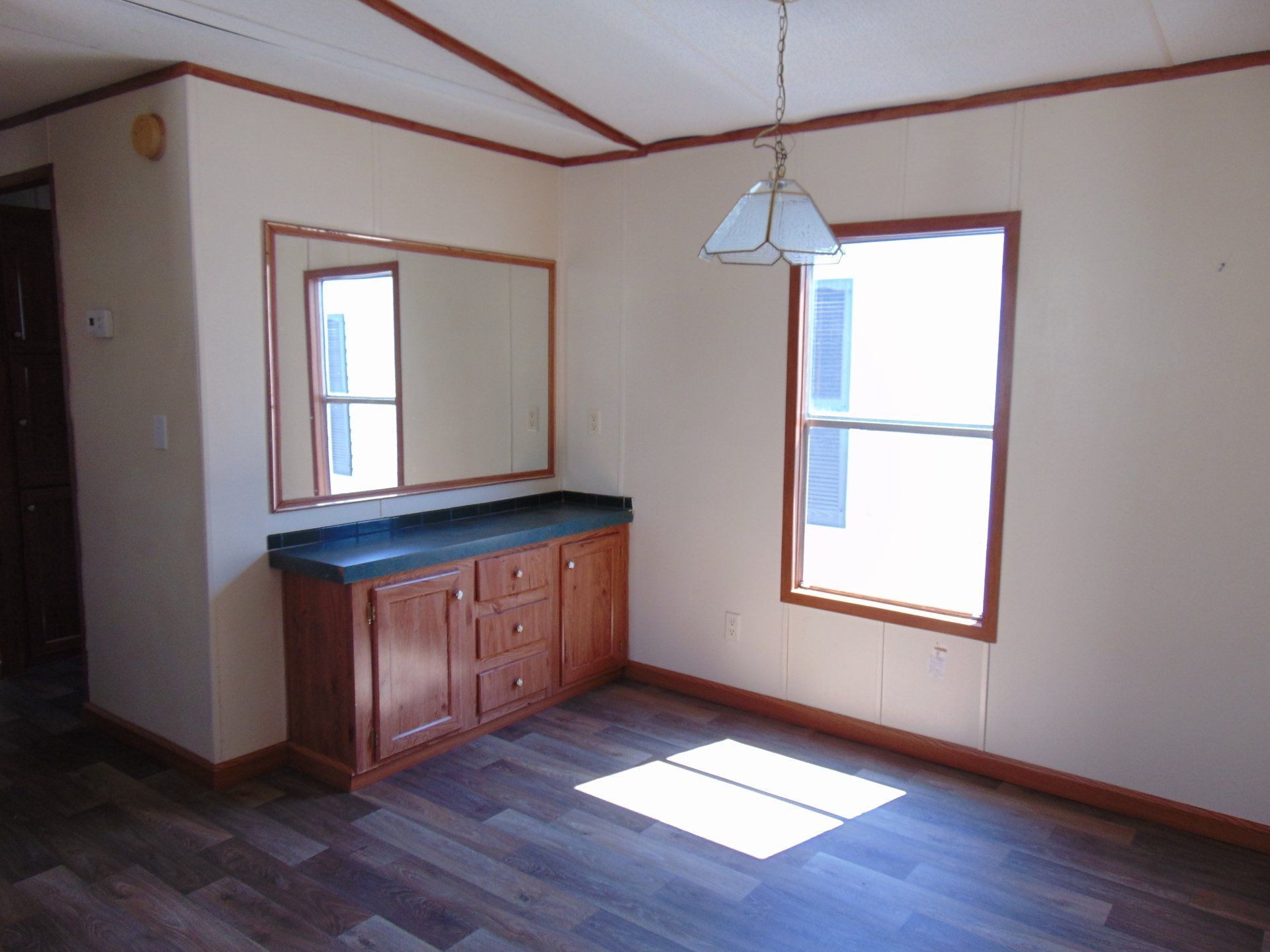 An empty dining room with a mirror and two windows