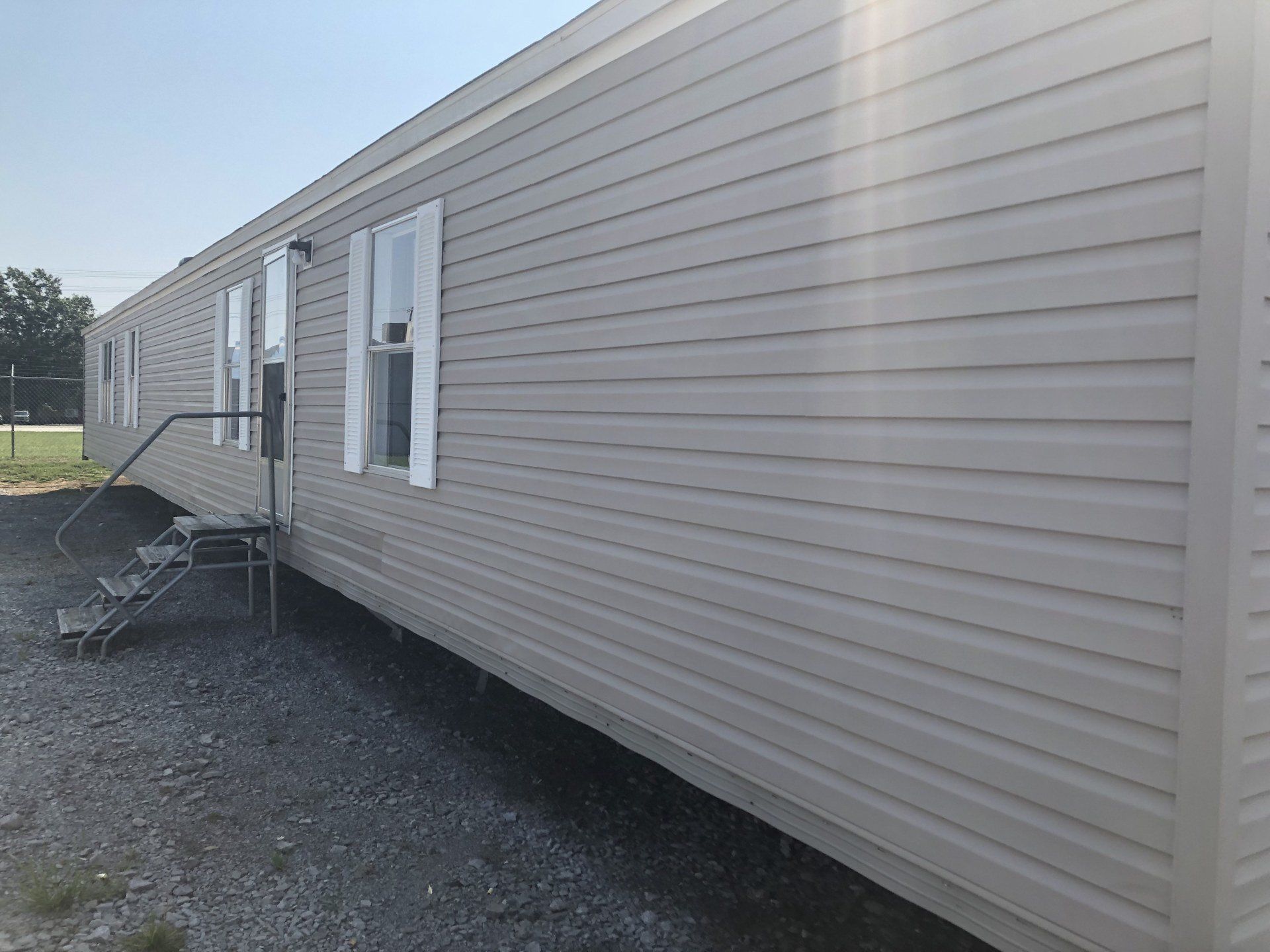 A mobile home with stairs leading up to it is parked in a gravel lot