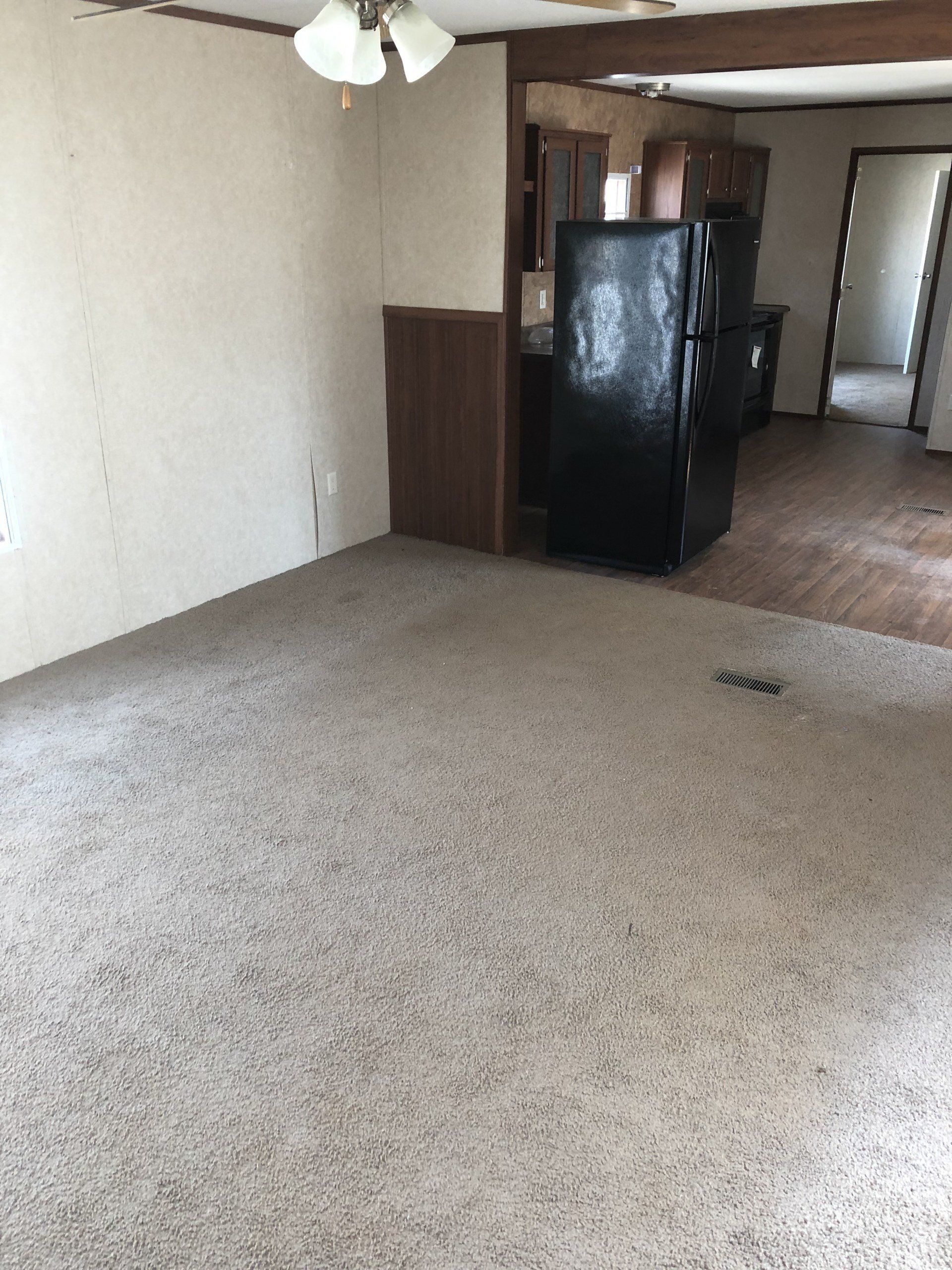An empty room with a black refrigerator and a ceiling fan