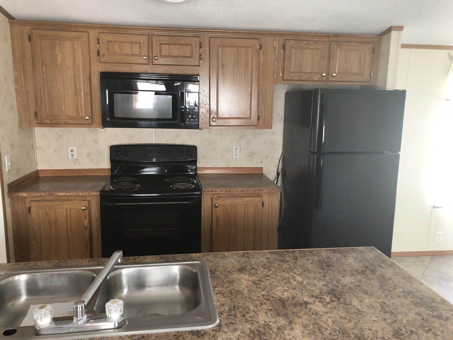 A kitchen with a sink, stove, microwave and refrigerator