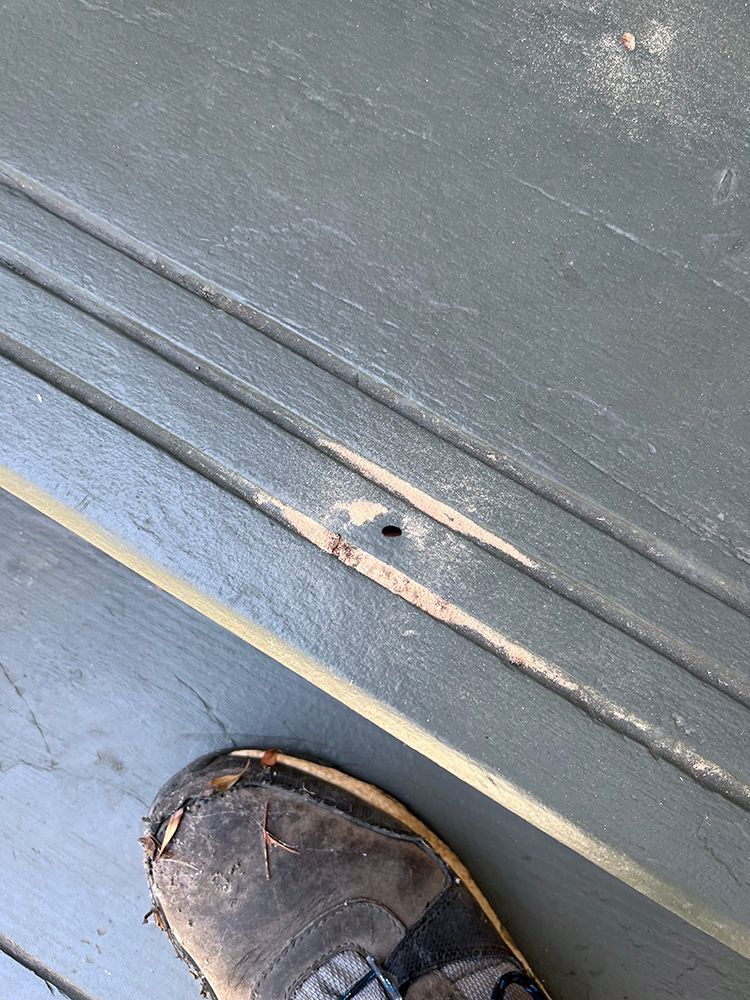 A person 's foot is standing on a wooden floor next to a door with a hole in it.