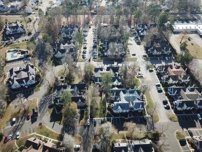 Aerial view of a suburban neighborhood with rows of houses, trees, and parked cars on a sunny day.