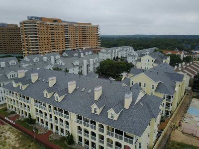 Aerial view of yellow multi-story apartment buildings with grey roofs, near a beach under a cloudy sky.