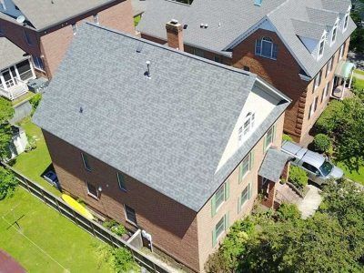 Brick building with gray shingle roof, small triangular window, and a white panel; van parked outside.