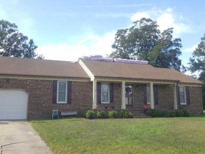 Brown brick house with shingles, porch, and insulation on the roof under a blue sky.