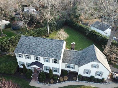 Aerial view of a white two-story house with gray roof, surrounded by green lawn and trees.