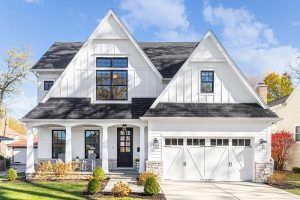 White farmhouse-style house with black accents, front door, and attached garage. Sunny day.