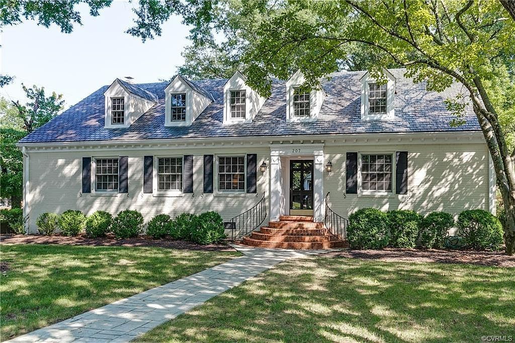 Beige house with black shutters and a brick walkway leading to the front door.