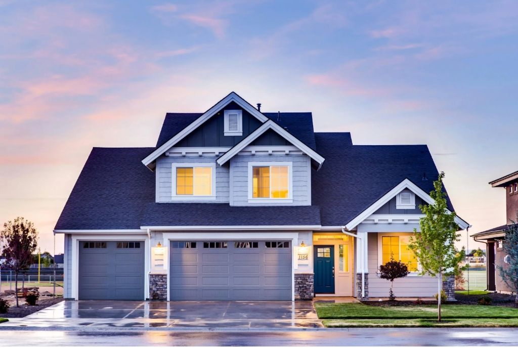 Two-story house with gray garage doors and blue siding. Evening sky in background.