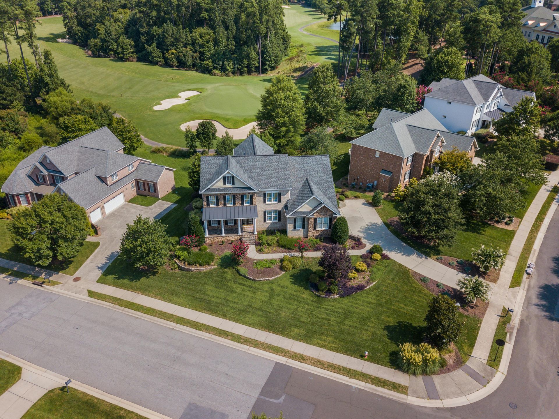Aerial view of suburban houses with manicured lawns and golf course in the background.