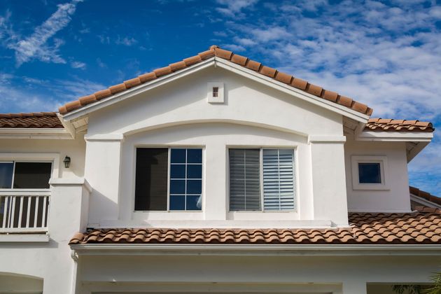 White stucco house with terracotta roof tiles against a blue sky.