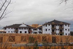 Buildings under construction, wrapped in white and brown, wooden frames in foreground, cloudy sky.