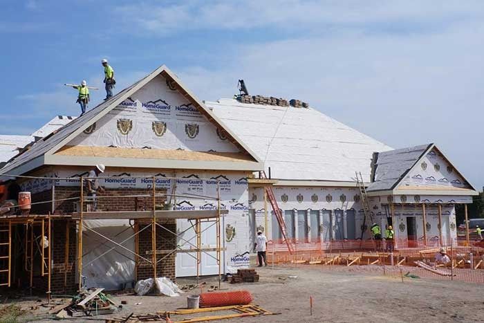 Construction workers on roof of a building, applying roofing materials under a blue sky.