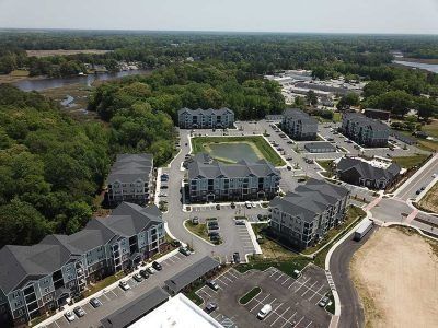 Aerial view of apartment complex with parking lots, surrounded by trees and a waterway.