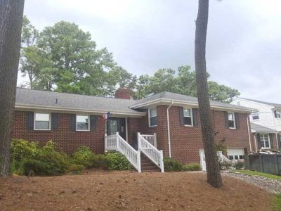 Brick house with white porch and steps; trees and cloudy sky.