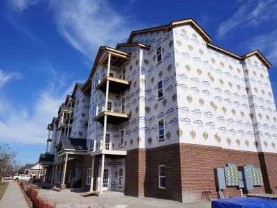 Multi-story building under construction with brick base, blue sky, and protective wrapping.